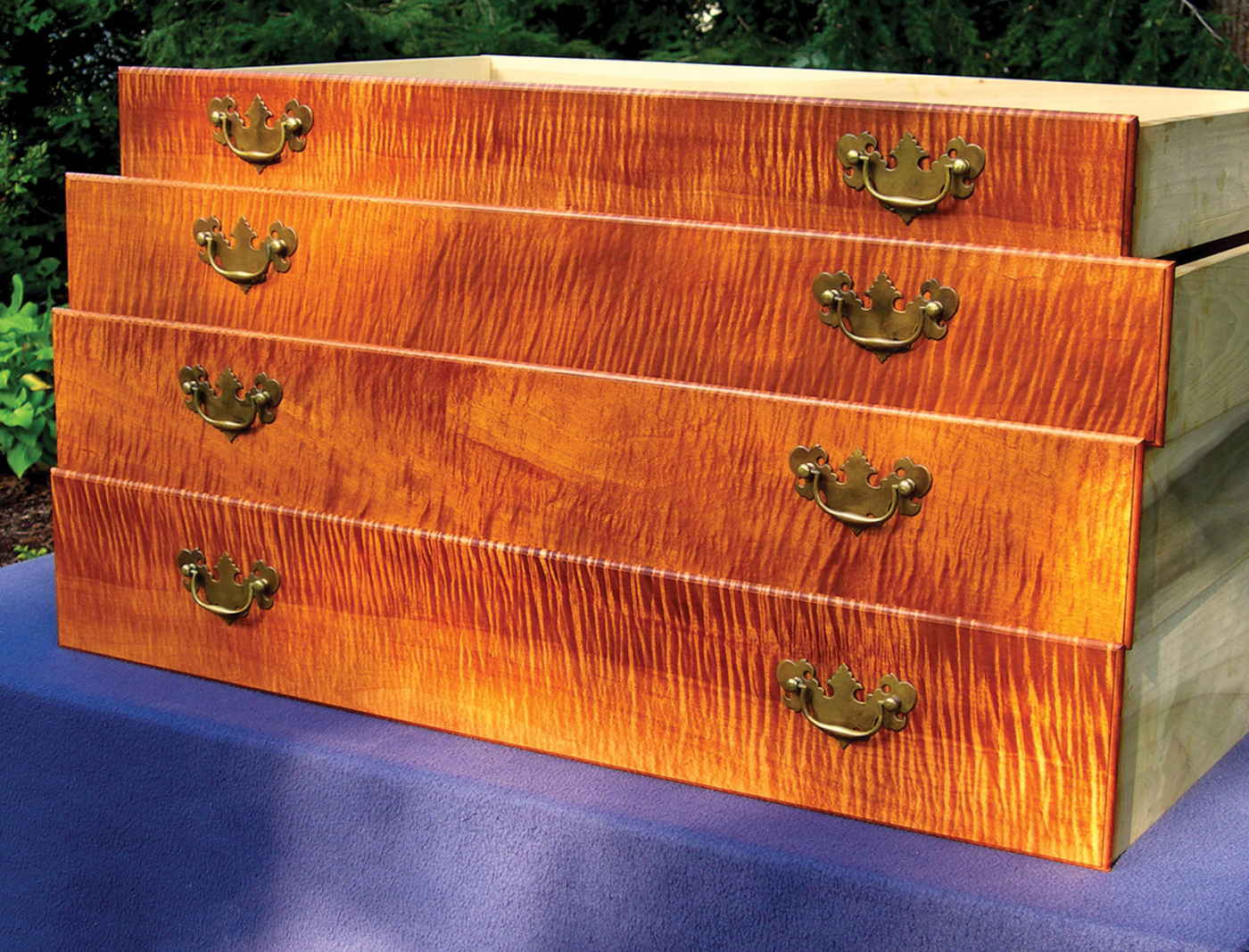 The right orientation adds shimmer and pop to your work.
by George R. Walker
pages 18-20
The barn loft was hot and dusty – and especially so after digging through piles of rough lumber for wide cherry boards at the bottom of the stack. We took a break outside for some fresh air and sat on a pile of firewood. I didn’t notice it right away, but the surface on the freshly split wood was deeply corrugated like a washboard and, to my horror, the whole woodpile was curly maple – wicked-good curly maple. The farmer seemed as disgusted as I was, but for a different reason. He held up a chunk of it and said, “This junk is a beast to split, burns good, but hardly worth the trouble.”
I’ll be the first to admit that figured maple, which includes tiger, curly, quilted and fiddleback grain, is ornery. The wavy grain and hardness is a challenge to split, carve or smooth with cutting tools. On top of that, the figure can be elusive: wild in one section of a board then suddenly going dead with no apparent reason.
Blog: Read more from George R. Walker on his Design Matters blog.
In our store: “Unlocking the Secrets of Traditional Design” and “Unlocking the Secrets of Traditional Design: Moldings,” DVDs by George R. Walker (Lie-Nielsen).