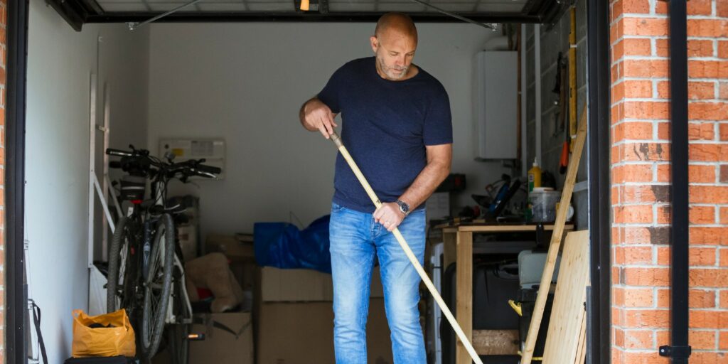 A man is sweeping the floor up his home garage with a large brush.