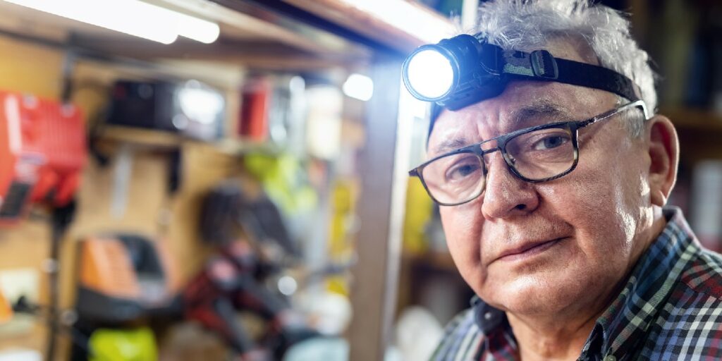 Senior craftsman portrait with headlamp led torch sitting in workhop with tools and equipment on background
