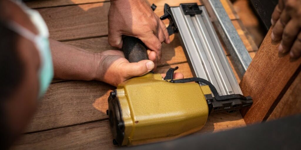 Closeup of a hand man carpenter using air nail gun to complete wood table in garden