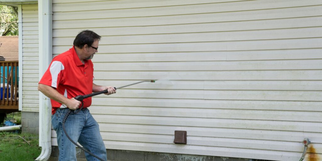 Contractor Using A Pressure Washer To Clean Vinyl Siding