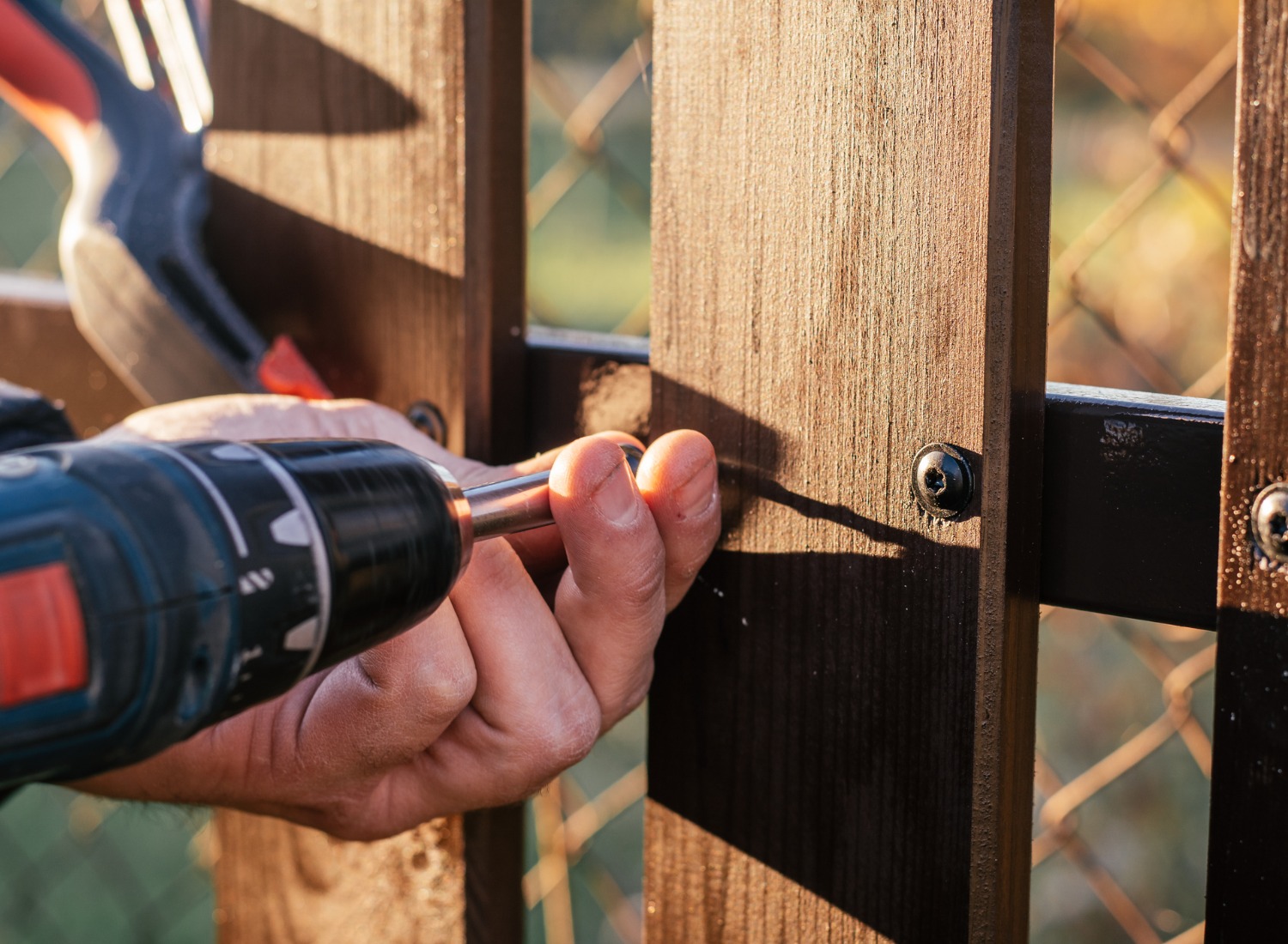 Man using a cordless drill to tighten screws on a fence